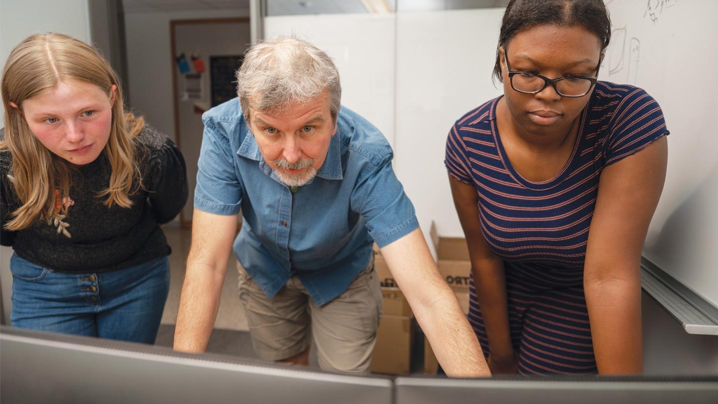 Hrbek (center) looks at a dual monitor while two students look on